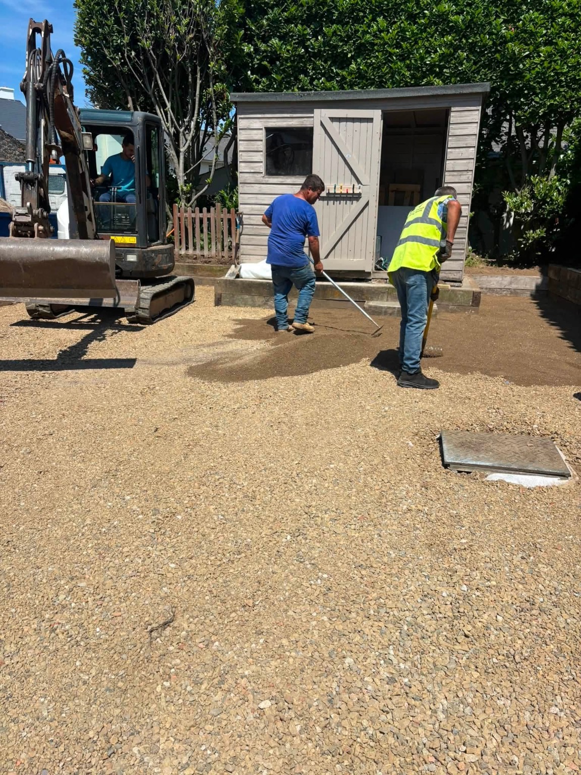 Workers preparing and levelling a ground base beside an excavator
