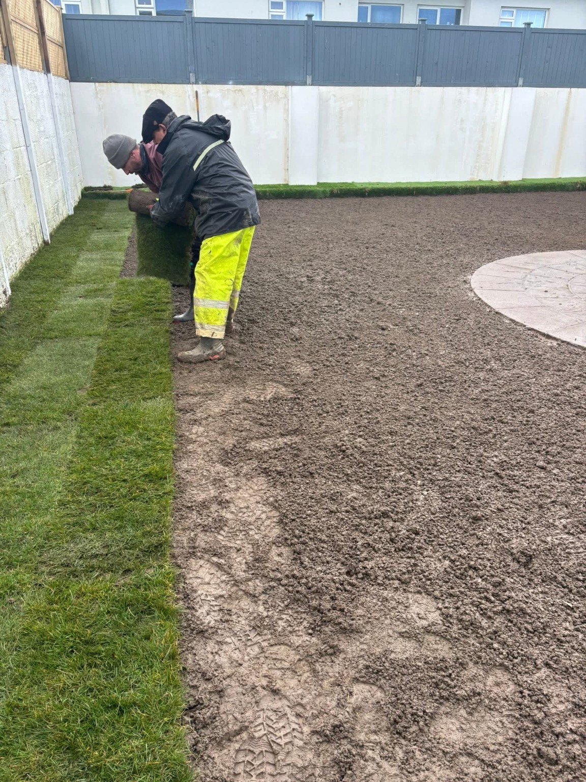 Workers laying lawn turf beside a patio